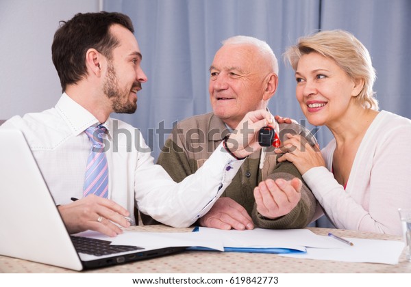 Aged couple\
signing papers for new car at home\
