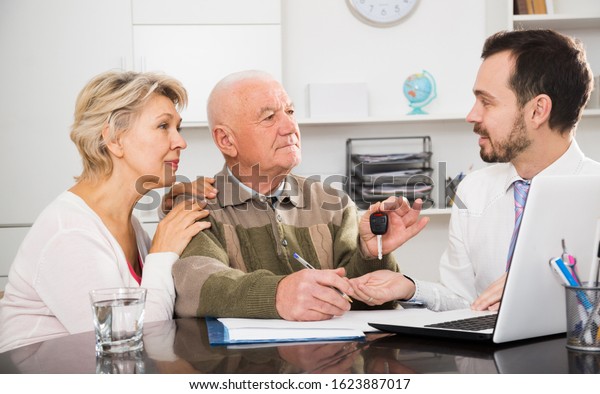 Aged\
couple signing papers to sell their car in bank\

