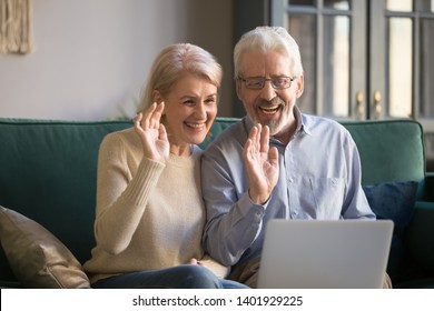 Aged couple sitting on couch in living room country house make videocall look at pc screen wave hands greeting friend, grown up children, grandchildren, modern tech and older generation users concept - Powered by Shutterstock