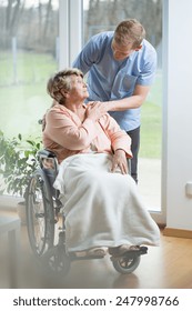 Aged disabled woman on wheelchair and her thoughtful male nurse