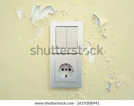 An aged electrical socket and light switch mounted on a wall with peeling paint