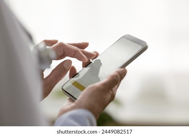 Aged female general practitioner holding modern smart phone in hands, close up screen view with white mock up, doctor working on-line, making calls, check schedule, jotting information, takes notes - Powered by Shutterstock