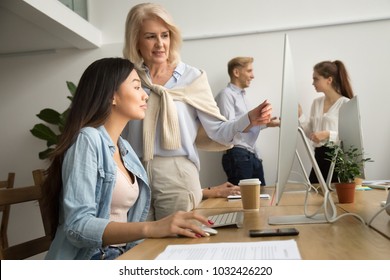 Aged Female Mentor Training Young Asian Intern Explaining Computer Work, Senior Friendly Executive Teaching New Employee Looking At Pc Screen, Older Teacher Talks To Student Helping With Online Task