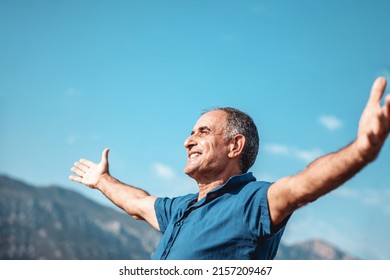 An aged happy smiling person standing with outstretched arms on mountains and blue sky background - Shutterstock ID 2157209467