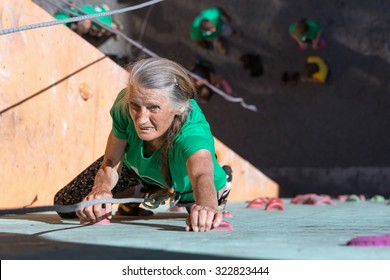 Aged Lady Doing Extreme Sport Elderly Female Makes Hard Move On Outdoor Climbing Wall Sporty Clothing On Fitness Training Intense But Positive Face Using Rope And Belaying Gear