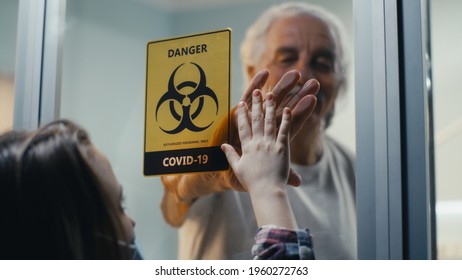 Aged Male Touching Hand Of Girl In Mask And Smiling While Standing Behind Glass Wall Of Coronavirus Ward In Hospital