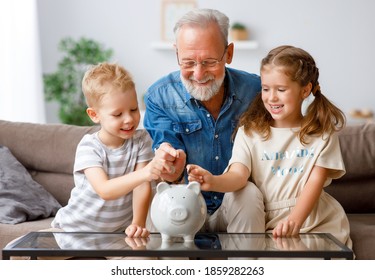 Aged man giving piggy bank to boy and girl while showing grandchildren how to save money at home