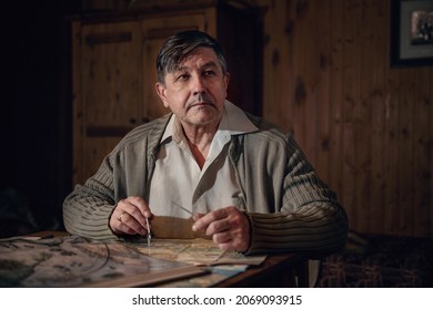 Aged Man Is Sitting Alone At Table In Front Of An Old Map Of Military Operations, Restoring Course Of Historical Events. Cinematic Style, Film Grain.