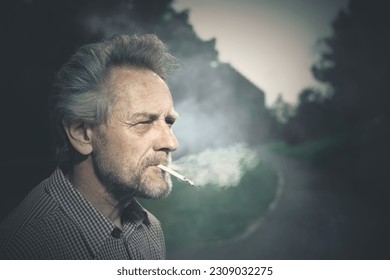 Aged man smoking cigarettes in city park lately on day time
