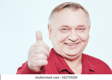 Aged Man Wearing Red Shirt Showing Thumb Up Hand Gesture And Smiling Against White Background - Happy Retirement Concept