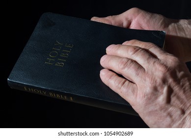 Aged Man's Hands Holding The Bible. Low Key Light.