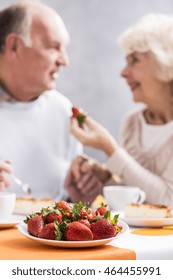 Aged Married Couple In Love Eating Strawberries. Older Woman Feeding Her Husband With A Red Fruit