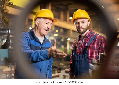 Aged master and his trainee in workwear and protective helmets consulting about new industrial machine equipment in workshop - Powered by Shutterstock