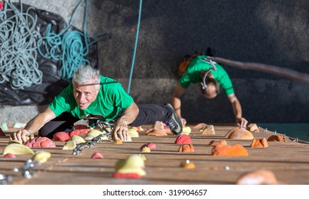 Aged Person Doing Extreme Sport Elderly Female Moving Up On Outdoor Climbing Wall Sporty Clothing On Fitness Training Intense But Positive Face Another Climber Start His Ascent On Background