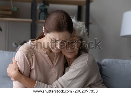Aged retired female mother hold in arms embrace tight upset depressed young female adult kid daughter listen to confession give excuse for wrong deed. Old lady mom support comfort beloved grownup girl