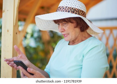 Aged Woman Talking On Phone. Old Lady In The Park. Sunny Day, Happy Mood. Upset Senior Woman With Phone