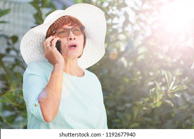 Aged Woman Talking On The Phone. Old Lady In Park. Sunny Day, Happy Mood. Upset Senior Woman With Phone