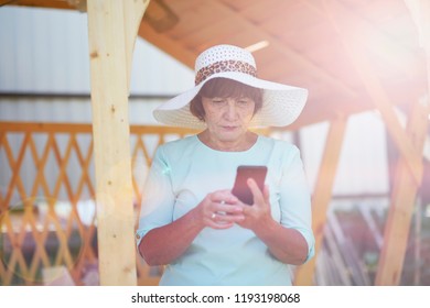 Aged Woman Talking On Phone. Old Lady In The Park. Sunny Day, Happy Mood. Upset Senior Woman With Phone