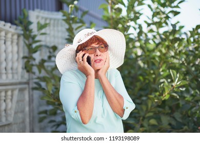 Aged Woman Talking On Phone. Old Lady In Park. Sunny Day, Happy Mood. Upset Senior Woman With Phone