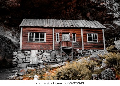 An aged wooden cabin with stone foundations nestled against the rocky cliffs of Jossingfjord, Norway. - Powered by Shutterstock