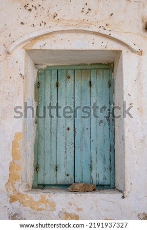 Aged wooden closed shutters with rusty hinges, peeled building wall facade. Abandoned house, stone keep the faded blue window planks shut. Vertical