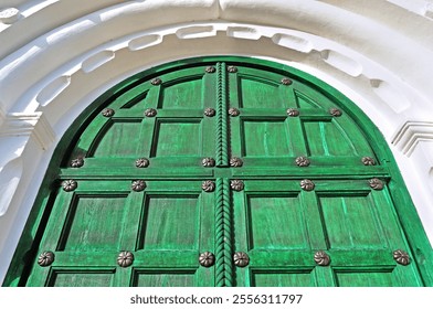 Aged wooden door of bright green color with metal rivets and upper arch made of white stone - vintage architecture background with old wooden door - Powered by Shutterstock