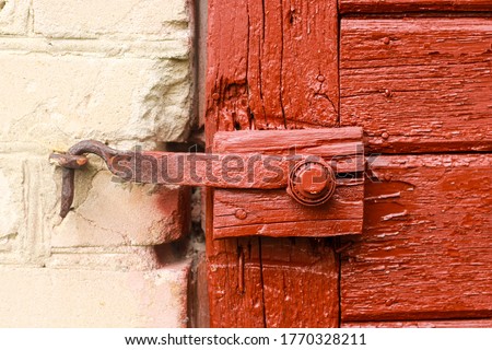 Aged wooden door with old rustic ironmongery, shackle, hasp & staple.  Red door. 
