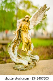 A Aged Yellow Angel Grave Statue On A Grave. It Was White At One Time, And The Alabaster Turned Yellow. The Statue Has A Broken Wing On The Left Side. 