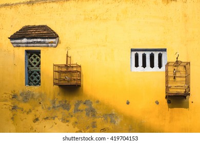 Aged yellow wall with small window and bird cage