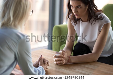 Aged and young women sitting staring at each other with distrust and animosity, focus on millennial girl. Different ages various generations employees conflict fight for company position or leadership