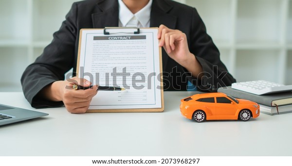Agent car female signing car insurance document or\
lease paper contract or agreement. Buying or selling new or used\
vehicle with car on\
table.
