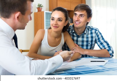 Agent explaining happy young couple details of insurance in home interior