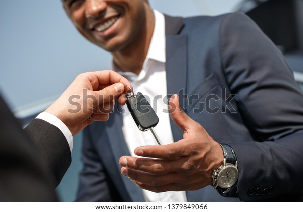 Agent giving key to\
young african american businessman standing near car smiling happy\
close-up bottom view