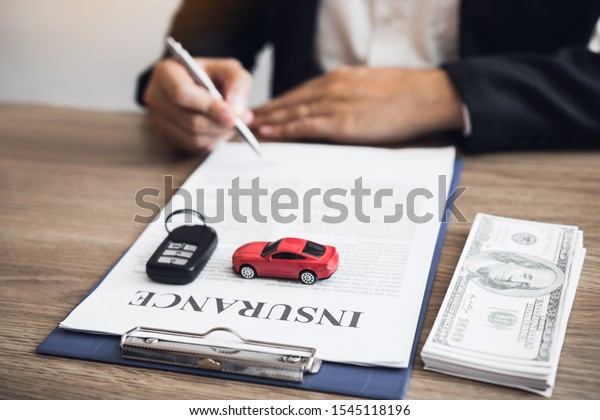 Agent is signing the insurance contract for the\
car at the document on the\
desk.