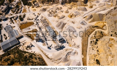Aggregate processing plant inside sand quarry from above. High angle drone frame shows conveyors, roof mounted solar panels, storage piles, trucks and access roads.