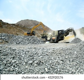 Aggregate Production By Mobile Crusher. Conveyor Belt Of A Working Mobile Crusher Machine. With Blown Away By The Wind White Stone Dust Against A Blue Sky. Mobile Crusher And Excavator