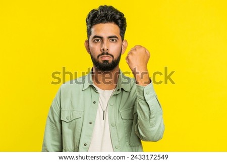 Aggressive angry Indian young man trying to fight at camera, shaking fist, boxing with expression, punishment, threaten, bullying, abuse, mad fury. Arabian guy isolated on yellow studio background