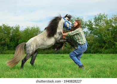 Aggressive Animal Is Attacking And Biting Young Woman In Her Neck In Outdoors, Side View. Caucasian Female Trainer Is Protecting Myself From Her Angry Horse.