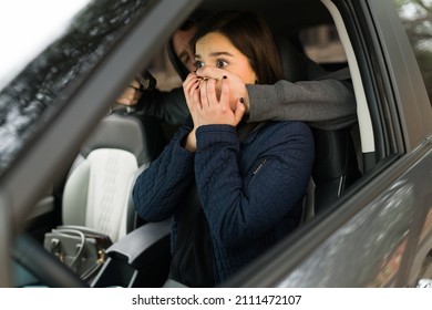 Aggressive criminal covering the mouth of his victim to stop her from screaming. Scared woman in the car abducted by a man with a gun