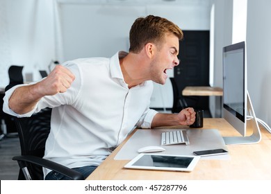 Aggressive furious young businessman shouting and working with computer in office