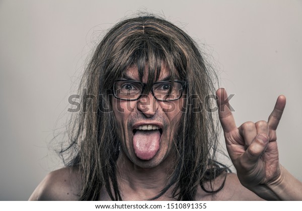 aggressive heavy metal music fan man with long hair\
makes devil sign and angry facial expression while head banging in\
the rhythm of hard\
rock
