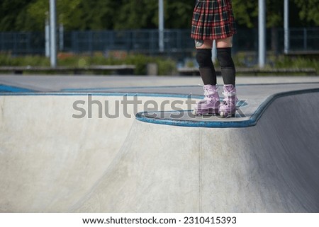 Aggressive inline skater girl wearing modern roller blades and protective knee pads and shin guards in a concrete skatepark. Cool young female athlete skating outdoor in a sunny summer day
