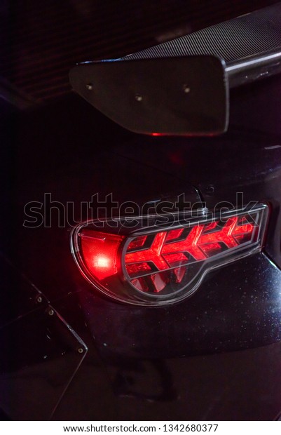 Aggressive looking red brake light\
of black sport car and a part of carbon fiber spoiler at\
night