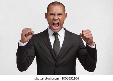 Aggressive mixed race young businessman has clenched fists, shouts loudly at coworkers, being dissatisfied with something, expresses irritation and negative emotions, very angry with someone