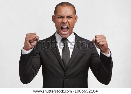 Aggressive mixed race young businessman has clenched fists, shouts loudly at coworkers, being dissatisfied with something, expresses irritation and negative emotions, very angry with someone