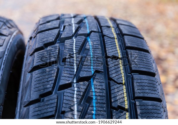 Aggressive non-symmetrical tread of car\
winter tire. Fragment of a new tire close-up at selective focus on\
a blurred\
background\
