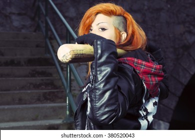 Aggressive punk woman posing with a baseball bat on stairs.