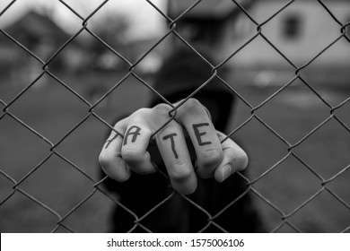 Aggressive teenage boy holding the wired fence at the correctional institute, the word hate is written on hes hand, conceptual image of juvenile delinquency in black and white. - Shutterstock ID 1575006106
