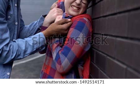 Aggressive teenager pushing nerd boy to wall, threatening physical harm bullying