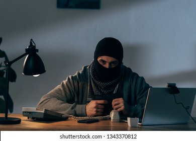 Aggressive Terrorist Sitting At Table With Gun And Looking At Camera